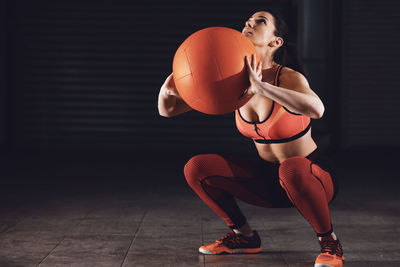 Full length of woman holding medicine ball and squatting in gym
