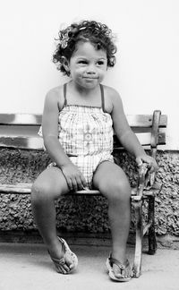 Cute girl sitting on bench against wall