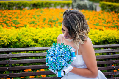 Bride holding bouquet while sitting on bench