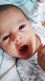 High angle portrait of cute baby girl yawning while lying on bed
