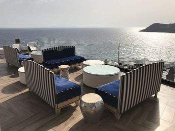 Chairs and table by swimming pool against sky on mykonos island 