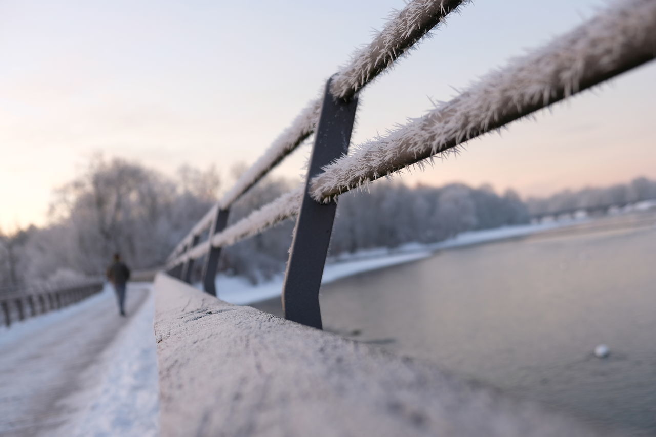 CLOSE-UP OF FROZEN RAILING BY BRIDGE AGAINST SKY DURING SUNSET