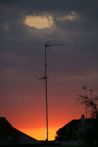 Low angle view of silhouette power lines against dramatic sky during sunset