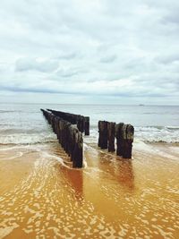 Wooden posts on beach against sky