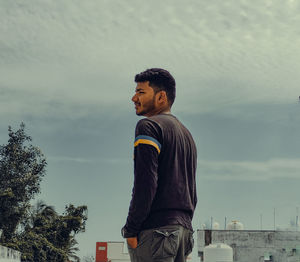 Side view of young man standing against sky