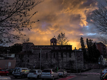 Cars on street by buildings against sky at sunset