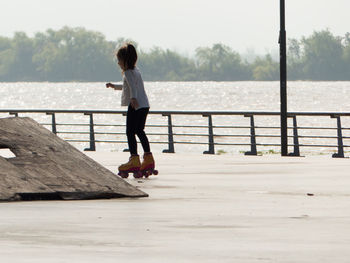 Girl roller skating on footpath against lake