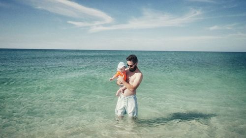 Man standing in sea with baby