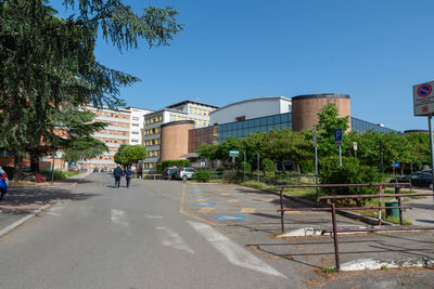 Road by buildings against clear blue sky