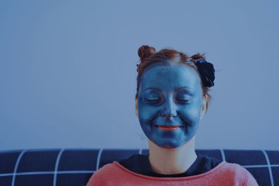 Close-up of young woman with beauty mask against blue wall