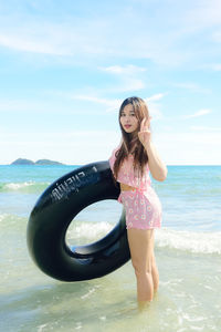 Portrait of young woman holding inflatable ring in sea against sky