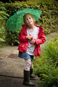 Full length of cute girl standing with umbrella on footpath