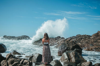 Woman standing on rock by sea against sky