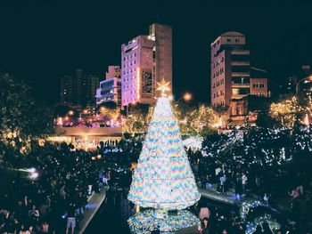 Rear view of people on illuminated street amidst buildings at night