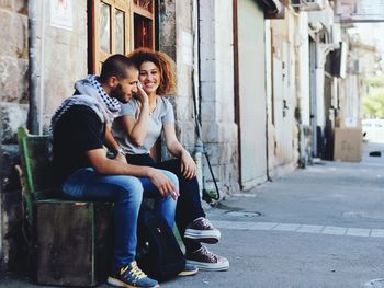 Full length of happy woman sitting on street in city