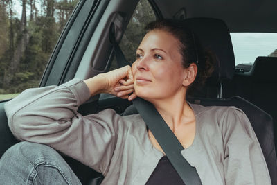 Woman looking away while sitting on car