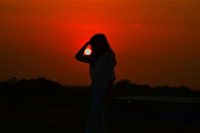 Silhouette woman standing on field against orange sky