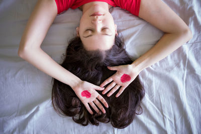 Directly above shot of woman with heart shape painted on hands at bedroom