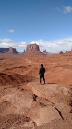 Rear view of man standing on rock in desert against sky