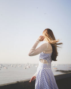 Rear view of woman standing at beach against clear sky