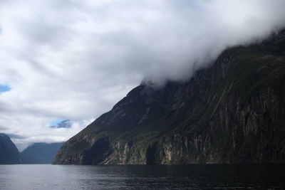 Scenic view of sea by mountain against sky