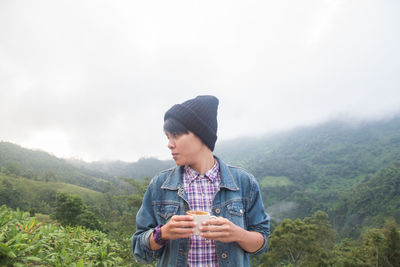 Young man holding ice cream against mountains