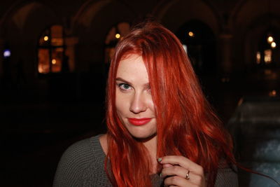 Portrait of beautiful woman holding hair while standing outdoors at night