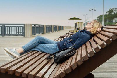 Woman on an empty city embankment rests with her eyes closed on a sun lounger. 