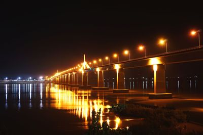 Illuminated bridge over river against sky at night