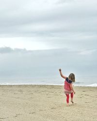 Rear view of girl walking on sand at beach against sky