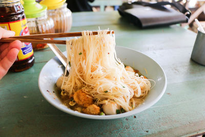 Close-up of hand holding noodles in bowl on table