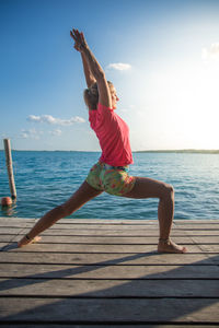 Full length of young woman exercising at beach against sky