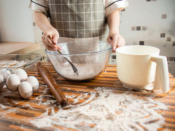 Woman in an apron in the kitchen prepares dough from flour, flour, eggs and a glass transparent bowl