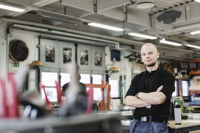 Portrait of confident male teacher standing arms crossed in high school workshop