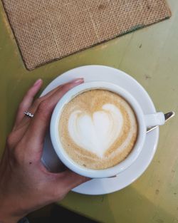 Cropped hand of woman holding coffee cup on table