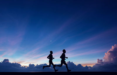 Silhouette athletes running on field against cloudy sky during sunrise