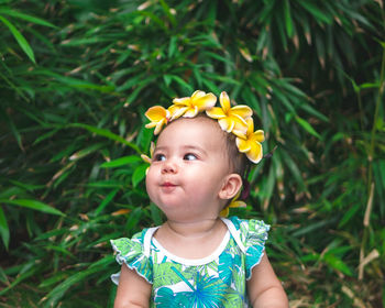 Baby girl wearing yellow frangipanis while looking away against plants