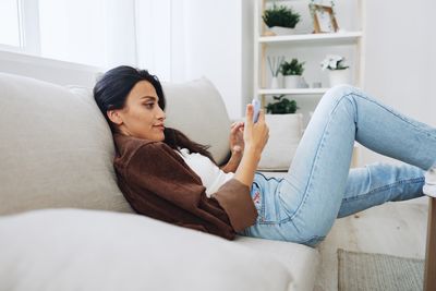 Young woman using mobile phone while lying on bed at home