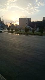 Road by buildings against sky during sunset in city