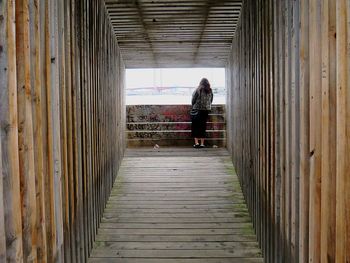Rear view of woman standing in covered wooden corridor