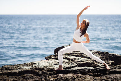 Full length of woman exercising on rock formation against sea