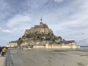 Historic building at beach against cloudy sky