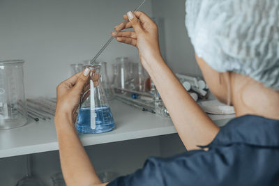 Female scientist  in cap, glass tube filled, blue chemical liquid, research, analysis in laboratory.