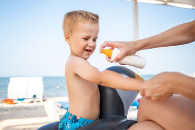 Midsection of father holding baby at beach against sky