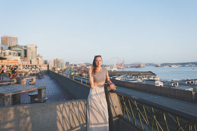 Portrait of beautiful woman standing on building terrace in city against clear sky