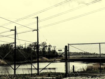 Electricity pylon by chainlink fence against sky