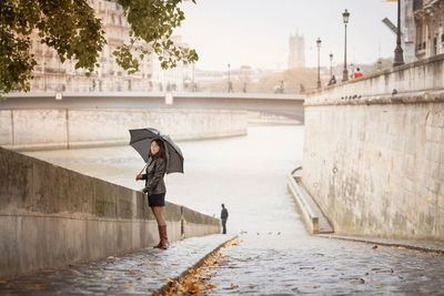 Brunette girl in a black jacket walks on the river embankment