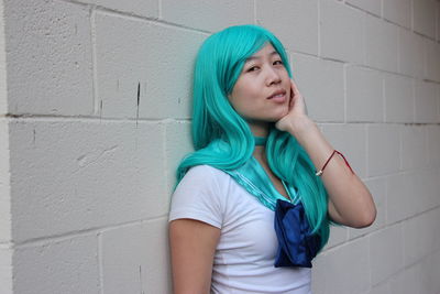 Portrait of woman with blue hair standing against wall