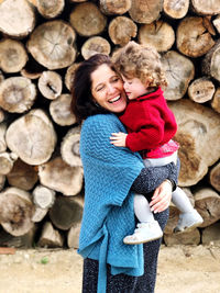 Smiling young woman carrying son against wooden log