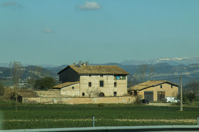 Houses on field by buildings against sky